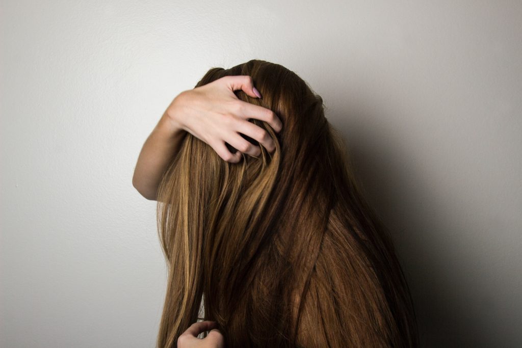 Zijaanzicht van vrouw met lang bruin haar die letterlijk met haar handen in het haar zit