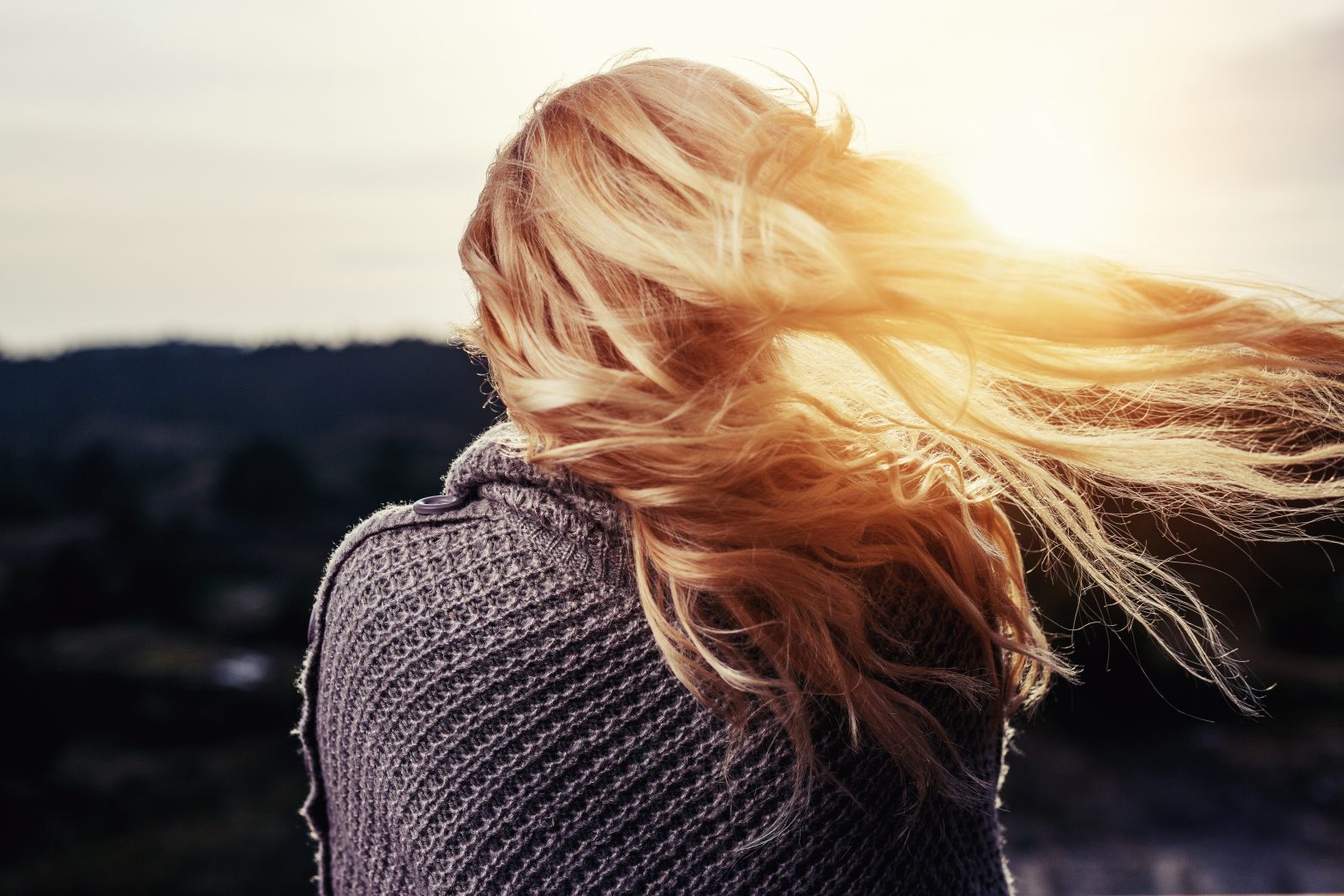 Achteraanzicht van een blonde vrouw met lang haar dat opzij waait.