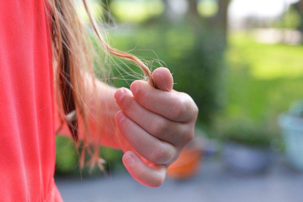 Close-up van een vrouw in een koraalroze jurk, die een pluk bruin haar vasthoudt.