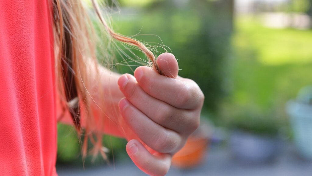Close-up van een vrouw in een koraalroze jurk, die een pluk bruin haar vasthoudt.